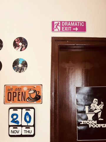Decorative street signs 'Dramatic Exit' on a wall next to a door.